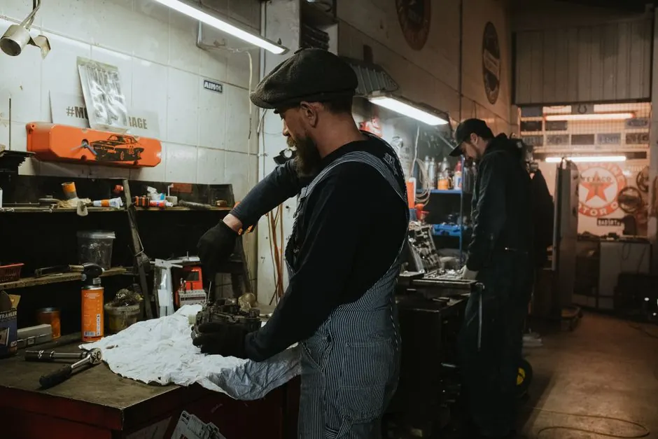Two auto mechanics engaged in vehicle repair work inside a dimly lit garage.